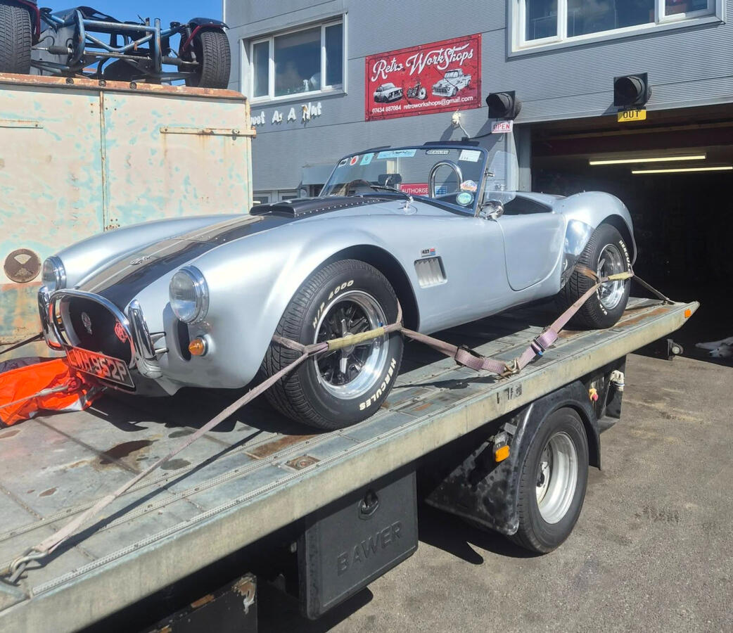 Silver AC Cobra with black stripe on car transported being delivered to workshop